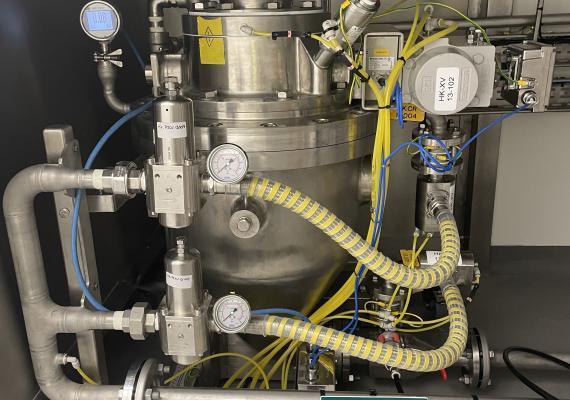 Front view of a stainless steel pneumatic transfer component, with pressure gauges, regulators, and yellow flexible pipes for conveying powders or granules.
