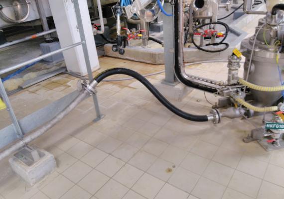 Connection of black flexible pneumatic transfer pipes and stainless steel pipes supported by a metal structure on the tiled floor.