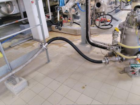 Connection of black flexible pneumatic transfer pipes and stainless steel pipes supported by a metal structure on the tiled floor.