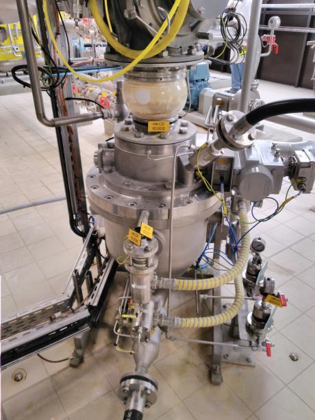 Stainless steel pneumatic distribution unit with transparent tank, labeled valves, and yellow flexible tubing for powder transfer.