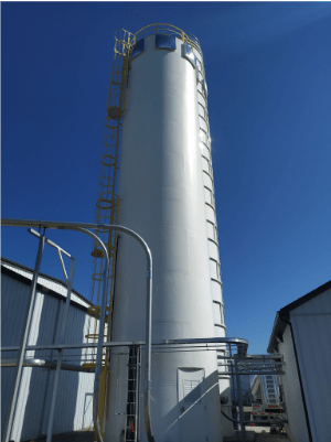 Silo rigide industriel blanc installé en extérieur, équipé d’une échelle et d’un garde-corps jaunes sous un ciel bleu clair.